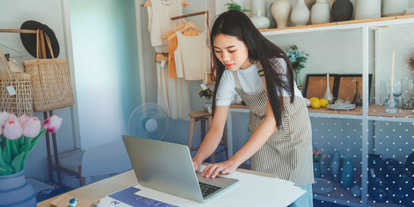small business owner standing in their shop while looking at a laptop and typing