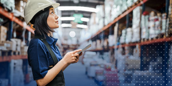 warehouse worker holding tablet and reviewing shelves stocked with product in warehouse
