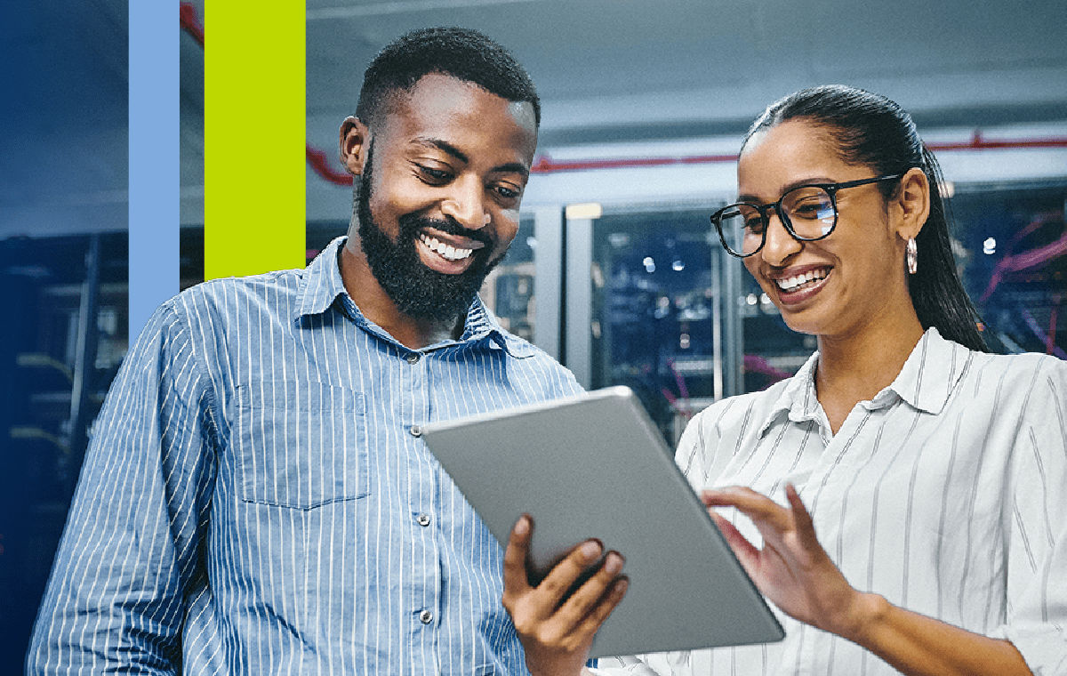 two coworkers standing in their office looking at a tablet while smiling