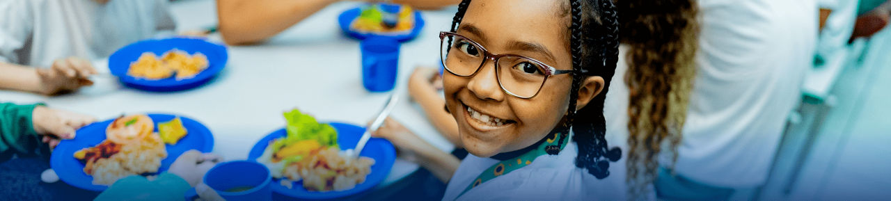 Child in school cafeteria smiling with school lunch