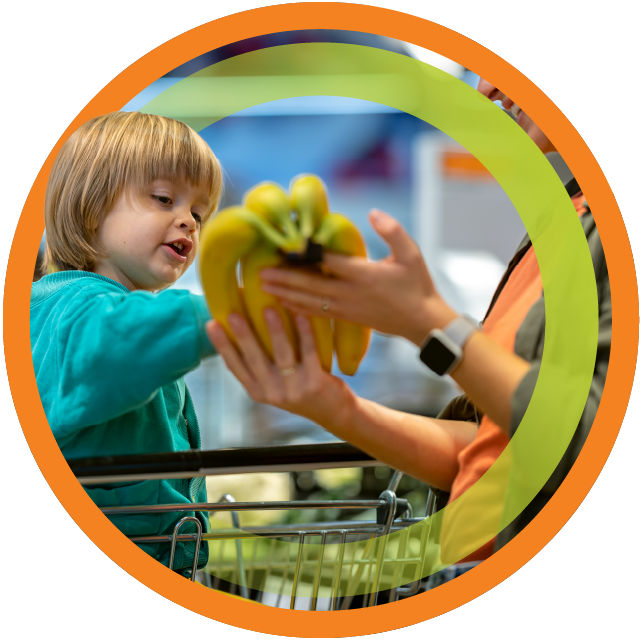 Child in grocery store cart holding bananas